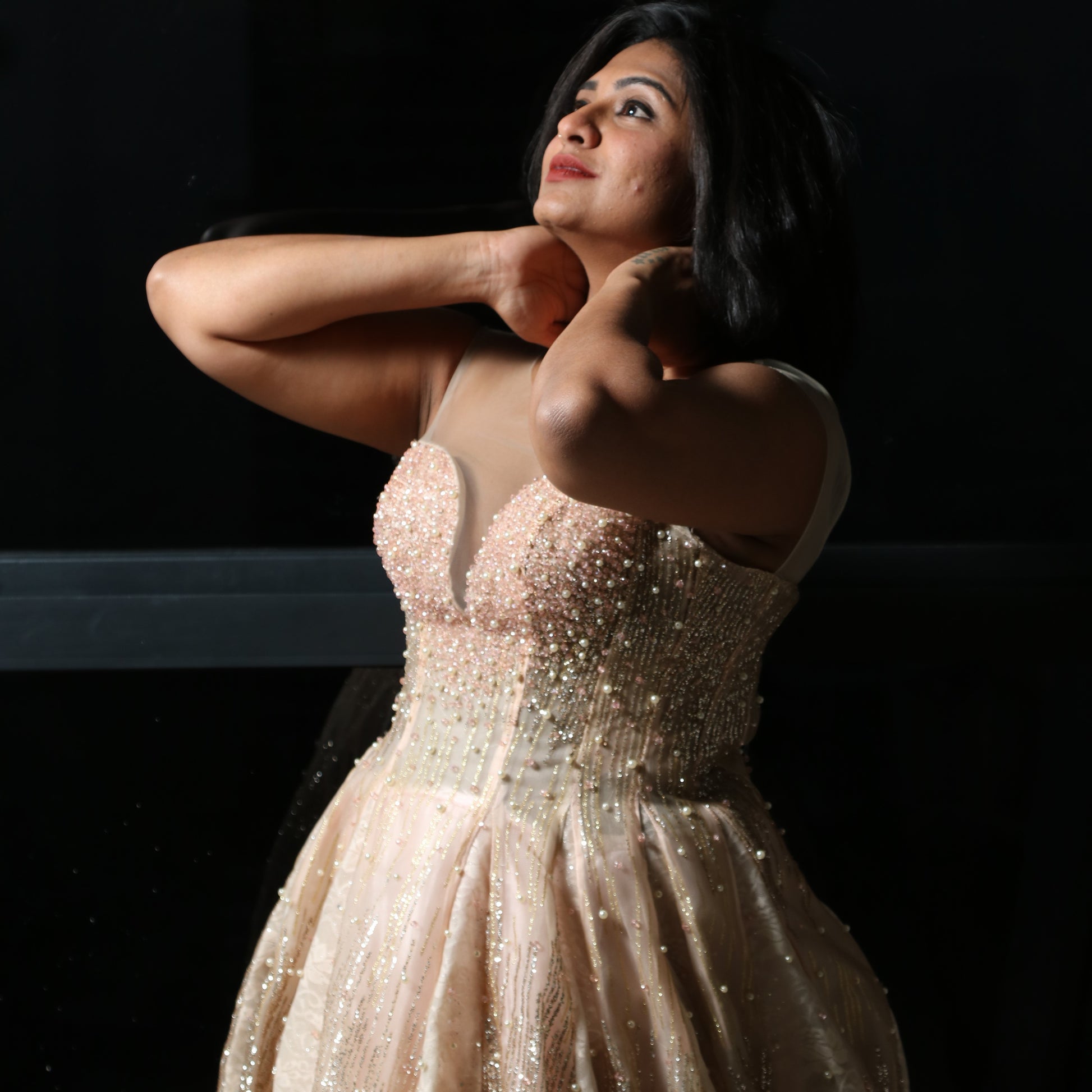The dress in the image is an elegant, heavily embellished gown with a fitted bodice and a voluminous skirt. It features intricate beadwork and embroidery, giving it a luxurious and opulent look. The sheer illusion neckline adds a delicate touch, while the structured, corset-like bodice enhances the silhouette. The fabric appears to be thick and richly adorned, making the dress quite heavy. The overall design exudes a regal and glamorous feel, perfect for a formal event or gala.