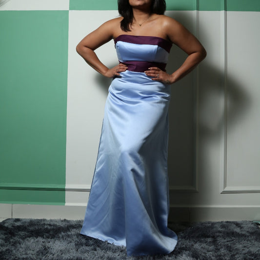 
This elegant evening dress is perfect for someone with a curvy figure, as it beautifully accentuates natural shape with its structured, strapless bodice and flowing floor-length satin skirt. The light blue fabric is complemented by a deep purple band across the bust and waist, creating a flattering color-blocked effect that enhances the silhouette. The design exudes sophistication and grace, making it an excellent choice for formal occasions