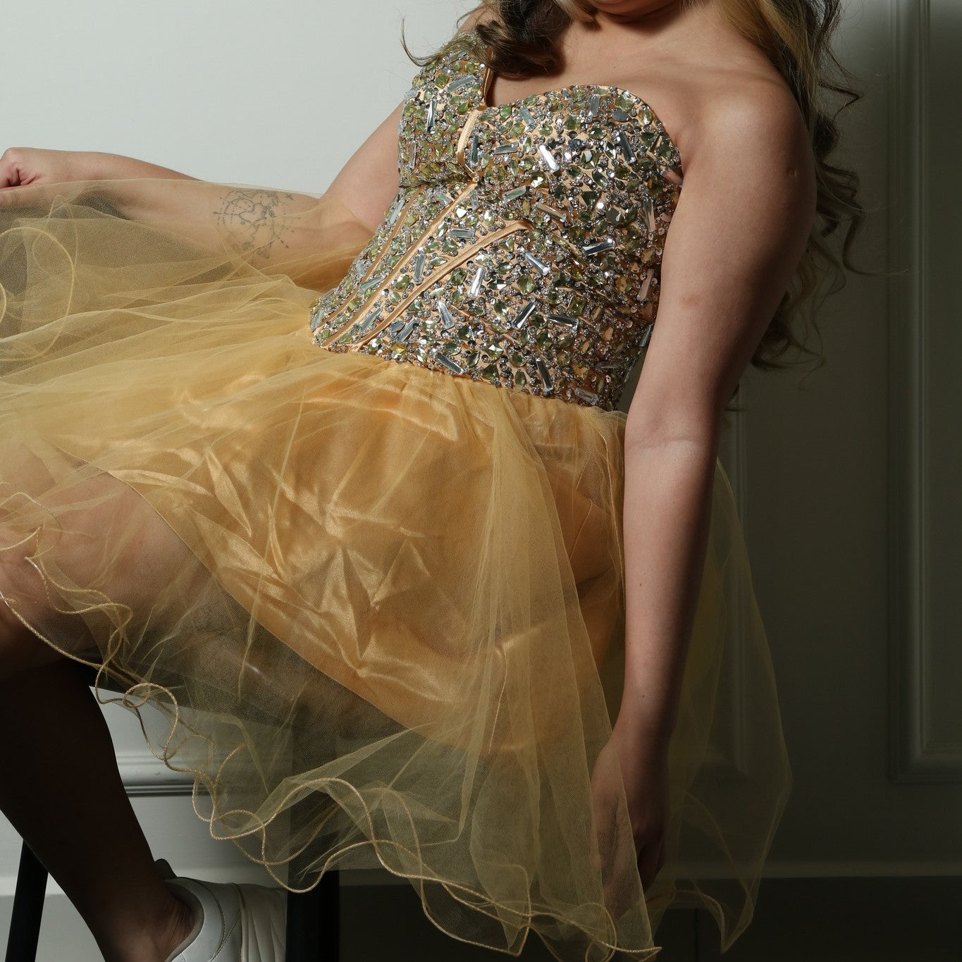 This is a glamorous party dress featuring a strapless sweetheart neckline and a fitted, heavily embellished bodice adorned with sparkling details. The structured corset-style bodice accentuates the waist, while the voluminous gold tulle skirt adds a playful and elegant touch. Perfect for special occasions, this dress combines sophistication with a fun and festive vibe.
