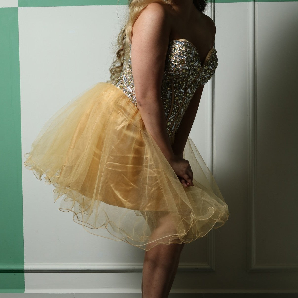 This is a glamorous party dress featuring a strapless sweetheart neckline and a fitted, heavily embellished bodice adorned with sparkling details. The structured corset-style bodice accentuates the waist, while the voluminous gold tulle skirt adds a playful and elegant touch. Perfect for special occasions, this dress combines sophistication with a fun and festive vibe.
