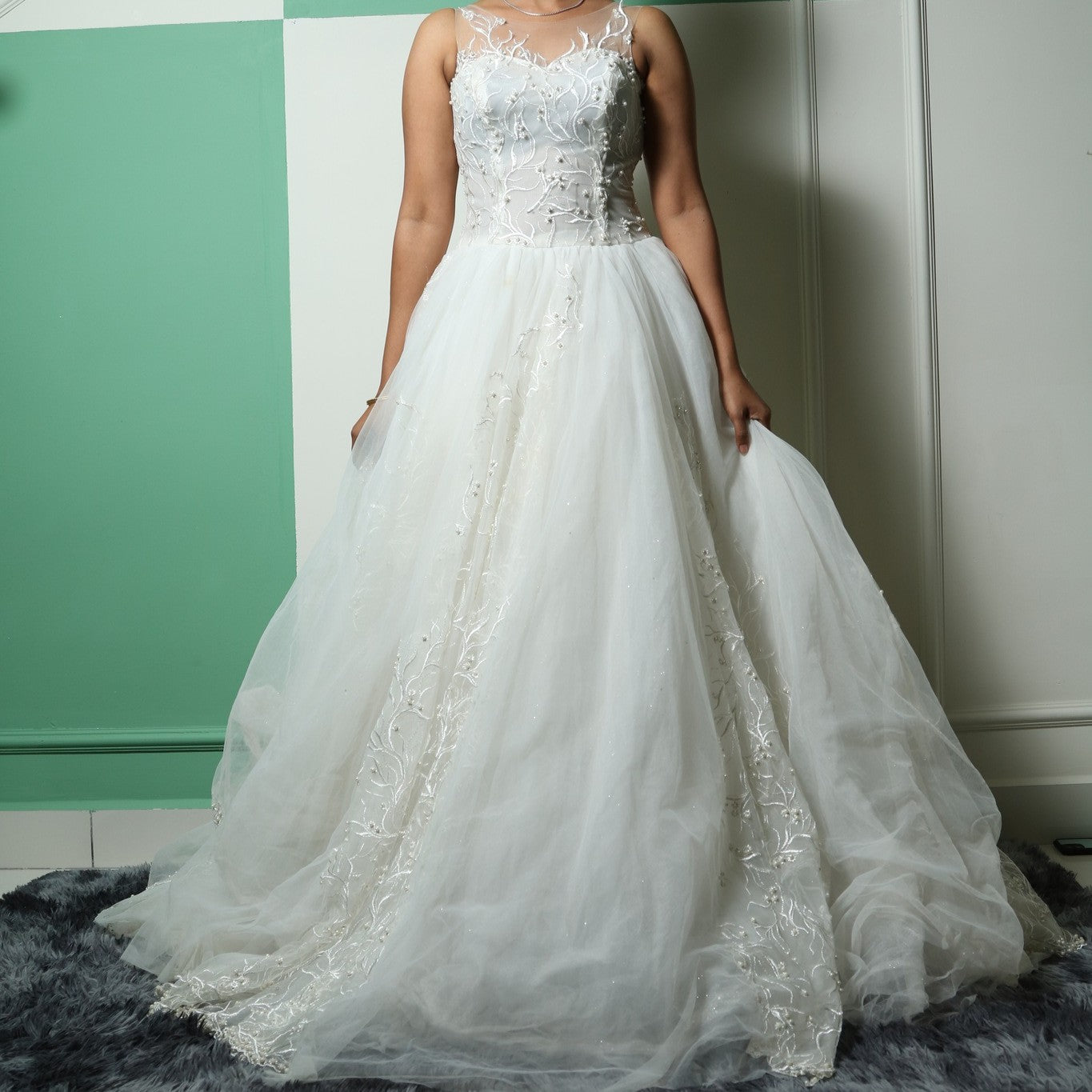 This wedding gown is a light and airy gown featuring a sheer illusion neckline and intricate floral embroidery on the bodice. The flowing tulle skirt is delicately adorned with subtle embellishments, adding an ethereal touch to its elegant silhouette.