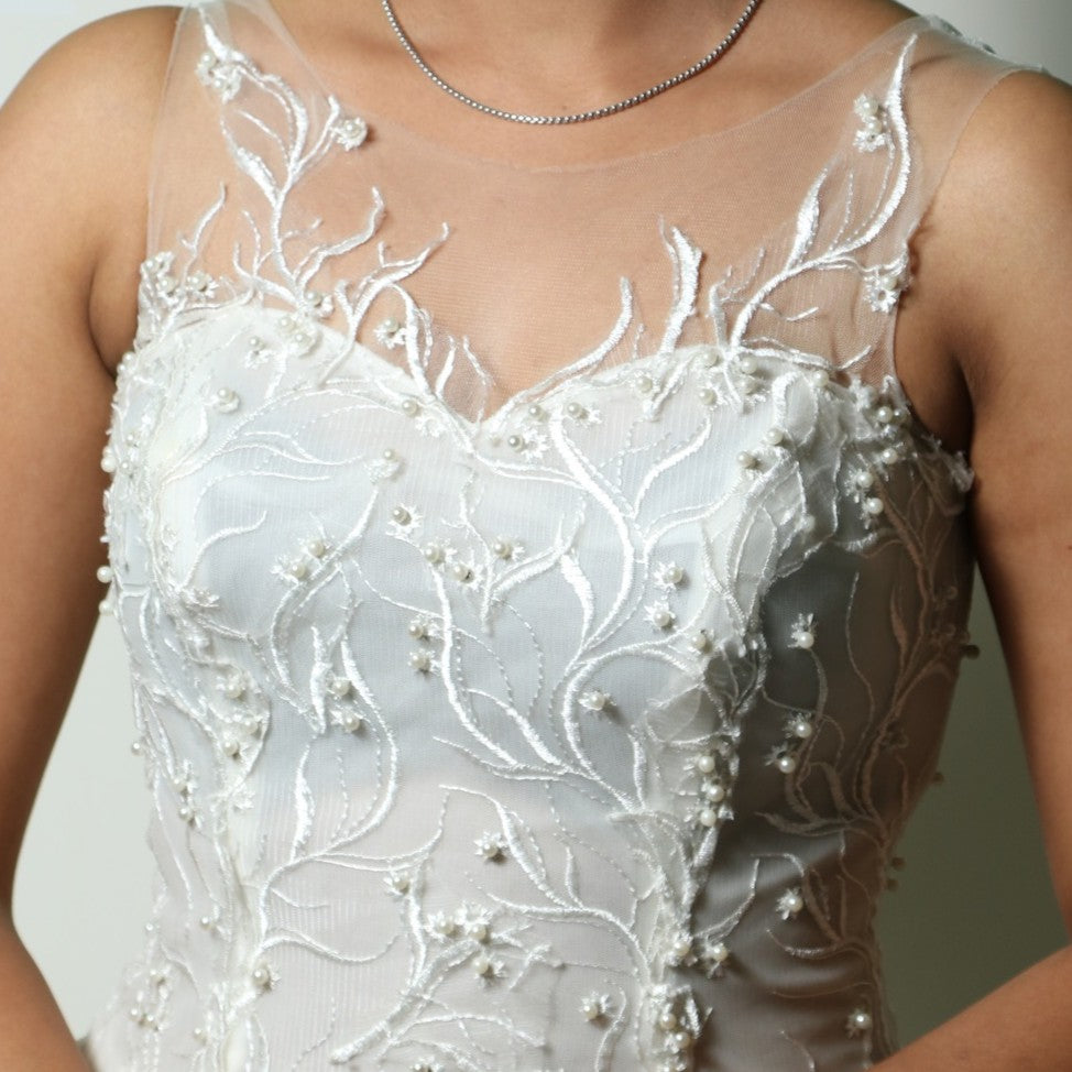 This wedding gown is a light and airy gown featuring a sheer illusion neckline and intricate floral embroidery on the bodice. The flowing tulle skirt is delicately adorned with subtle embellishments, adding an ethereal touch to its elegant silhouette.