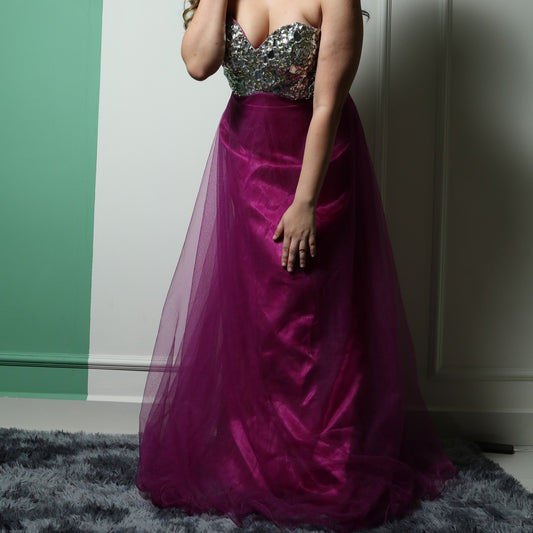 This dress features a strapless, sweetheart neckline bodice adorned with reflective silver embellishments, creating a glamorous and eye-catching effect. The voluminous skirt is made of rich magenta tulle, adding an elegant and dramatic touch. The combination of sparkle and flowy fabric makes it a perfect choice for formal events or evening wear.