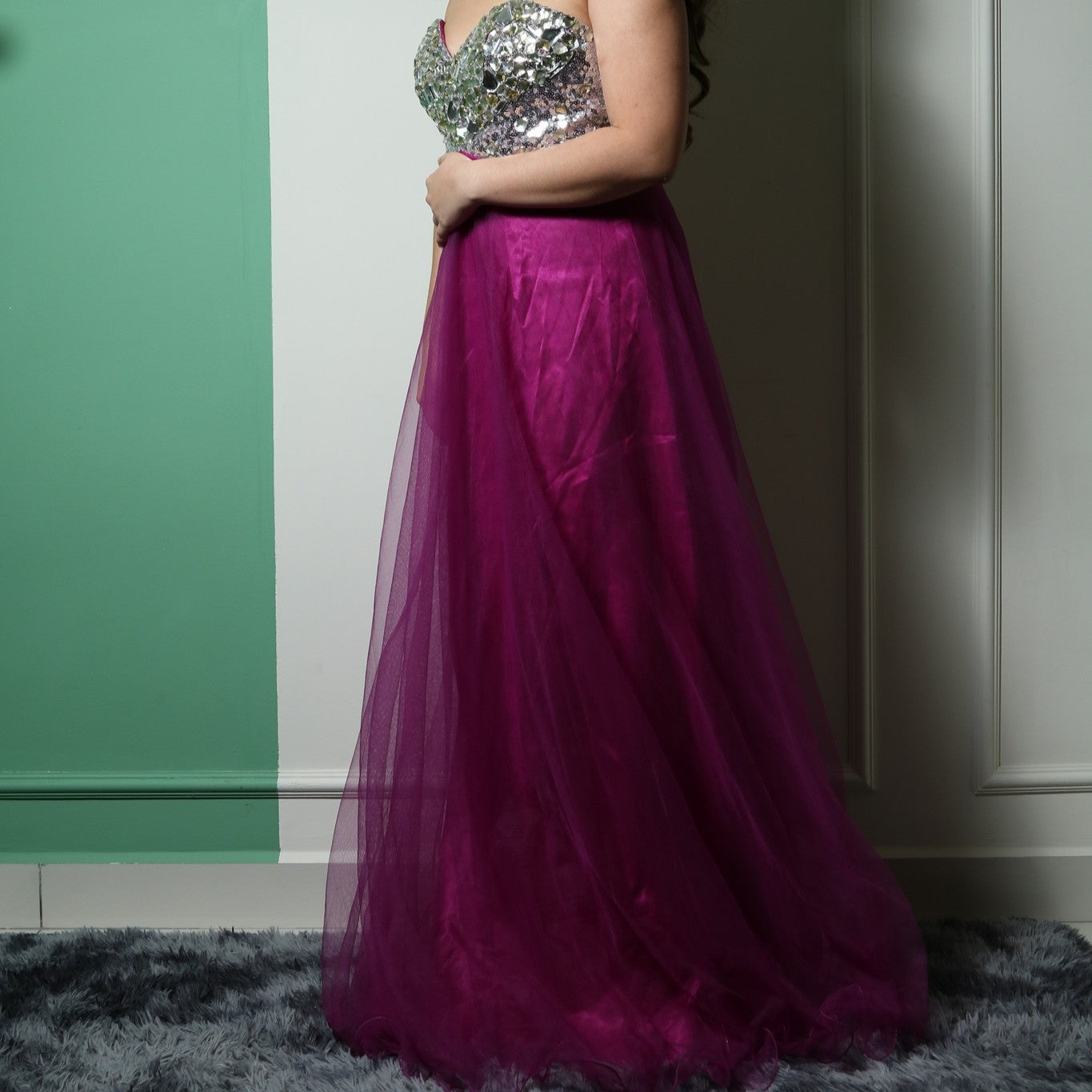 This dress features a strapless, sweetheart neckline bodice adorned with reflective silver embellishments, creating a glamorous and eye-catching effect. The voluminous skirt is made of rich magenta tulle, adding an elegant and dramatic touch. The combination of sparkle and flowy fabric makes it a perfect choice for formal events or evening wear.