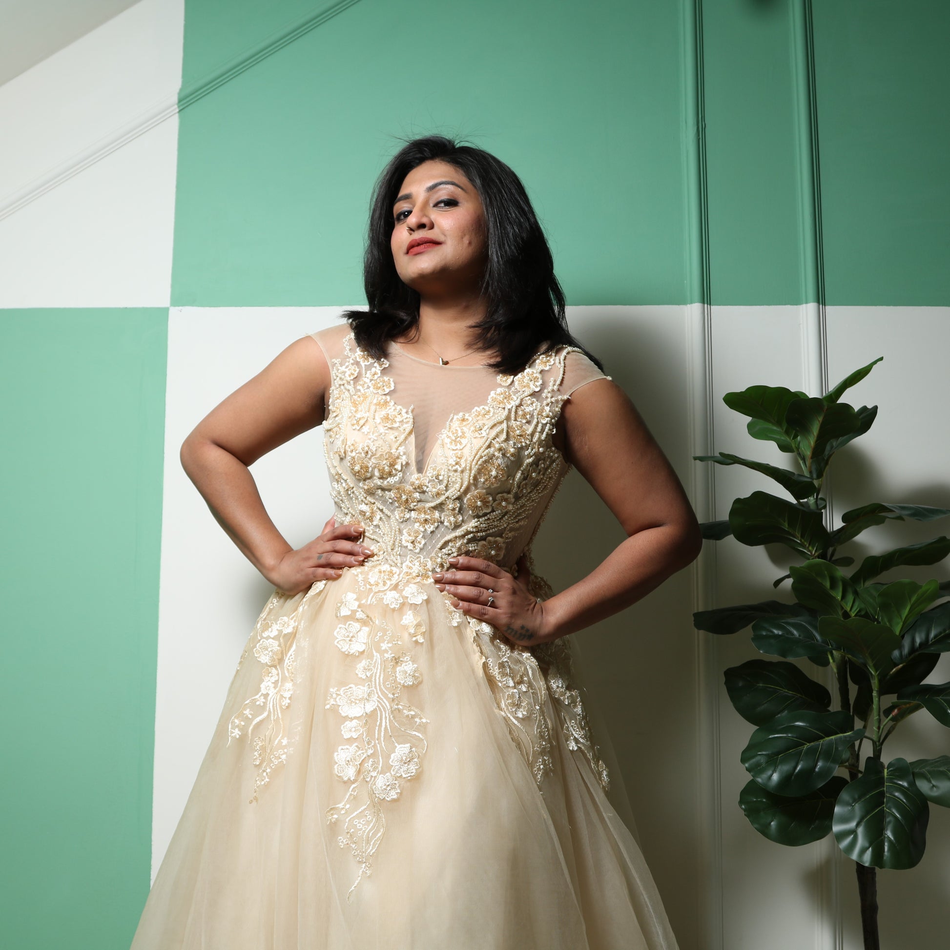The dress in the image is a floor-length gown in a soft champagne or gold color. It features a fitted bodice with intricate floral embroidery and beadwork, extending into delicate cap sleeves. The gown has a sheer illusion neckline, adding elegance and sophistication. The voluminous tulle skirt flows gracefully, creating a princess-like silhouette. This dress is perfect for formal events, weddings, or special occasions.