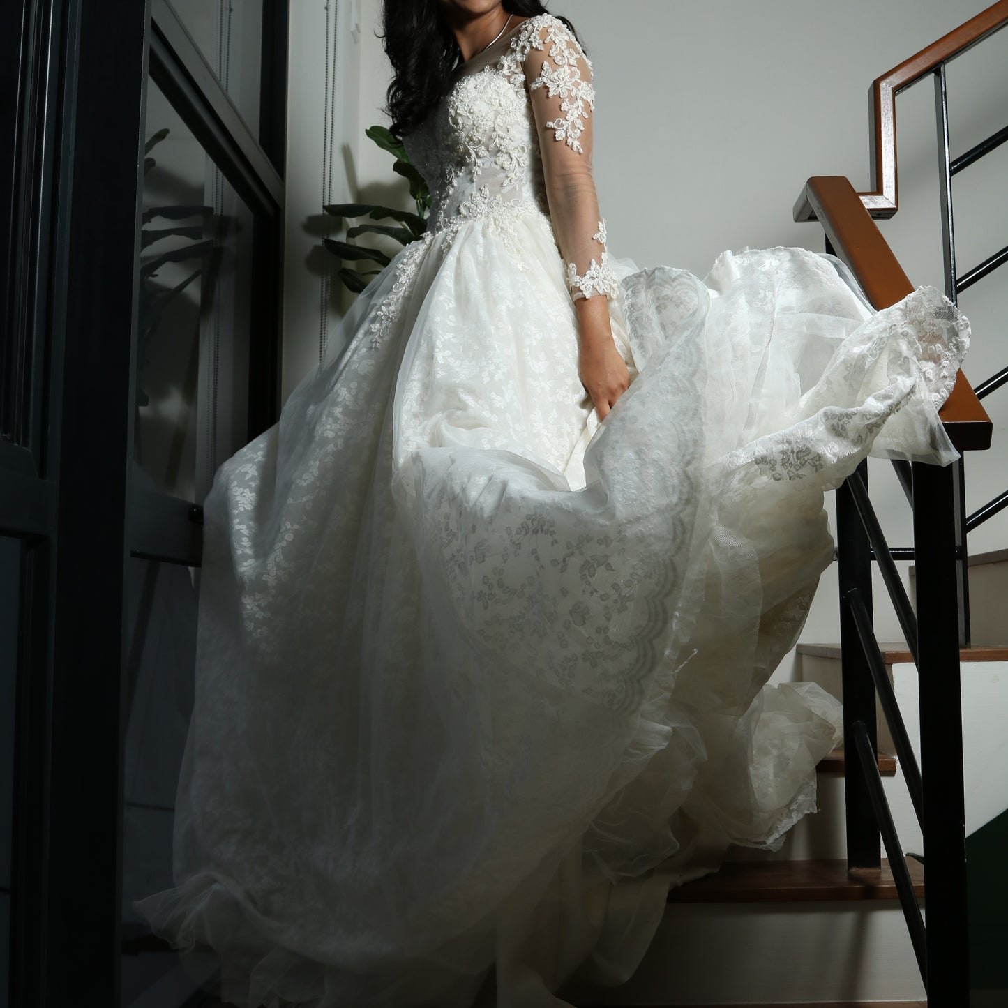 This wedding dress is an elegant A-line gown featuring a sheer illusion neckline, long lace-embellished sleeves, and a fitted bodice adorned with delicate floral lace appliqués. The voluminous skirt, crafted from soft tulle with lace detailing, adds a romantic and timeless touch, making it a perfect choice for a classic bridal look.