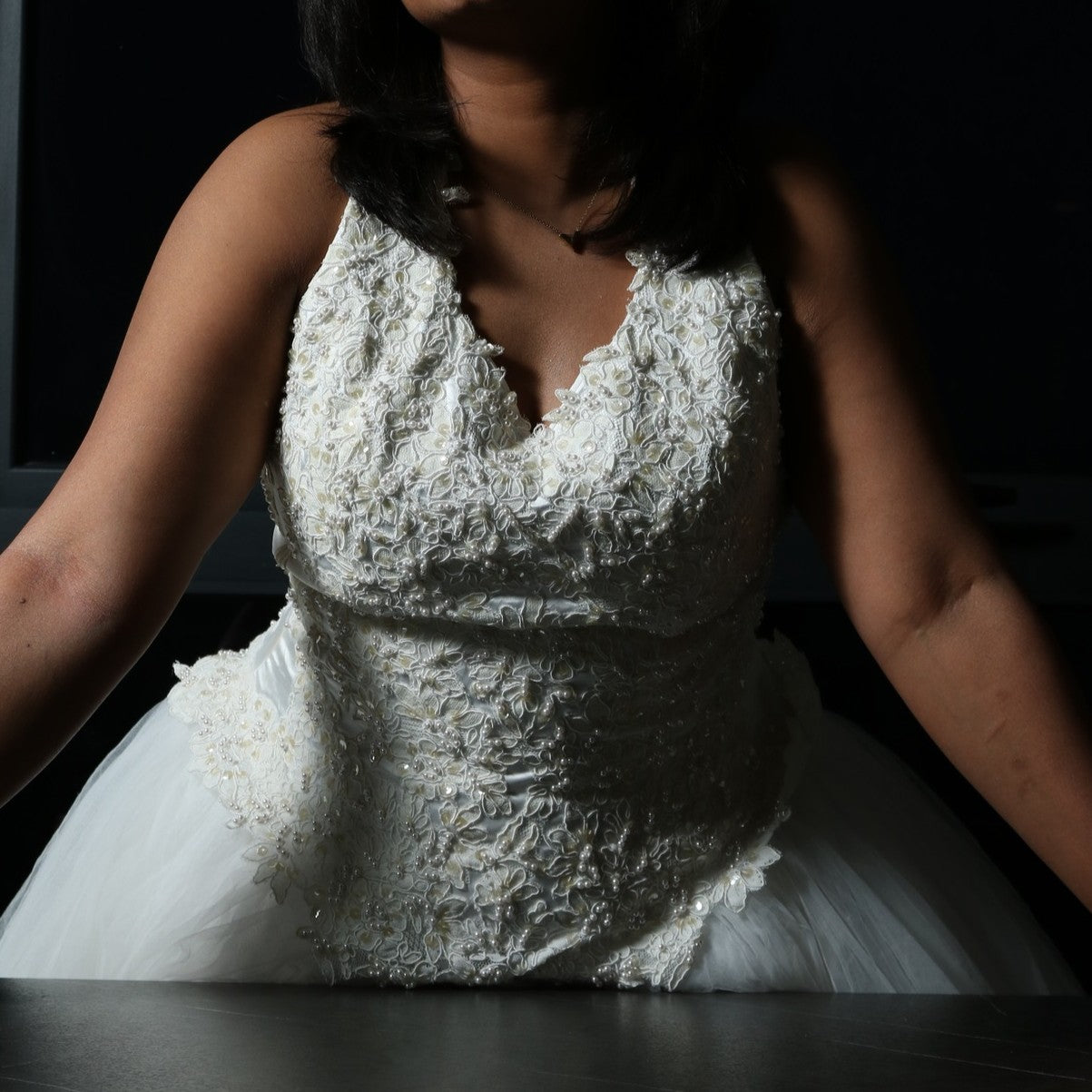 This dress is a stunning white gown with a voluminous tulle skirt, creating an ethereal and lightweight appearance. The bodice features intricate lace or beaded detailing with a flattering V-neckline and sleeveless design. The skirt is made of multiple layers of airy tulle, giving it a dreamy, floating effect. The overall look is elegant, romantic, and light, making it a perfect choice for a formal event such as a wedding or a gala.