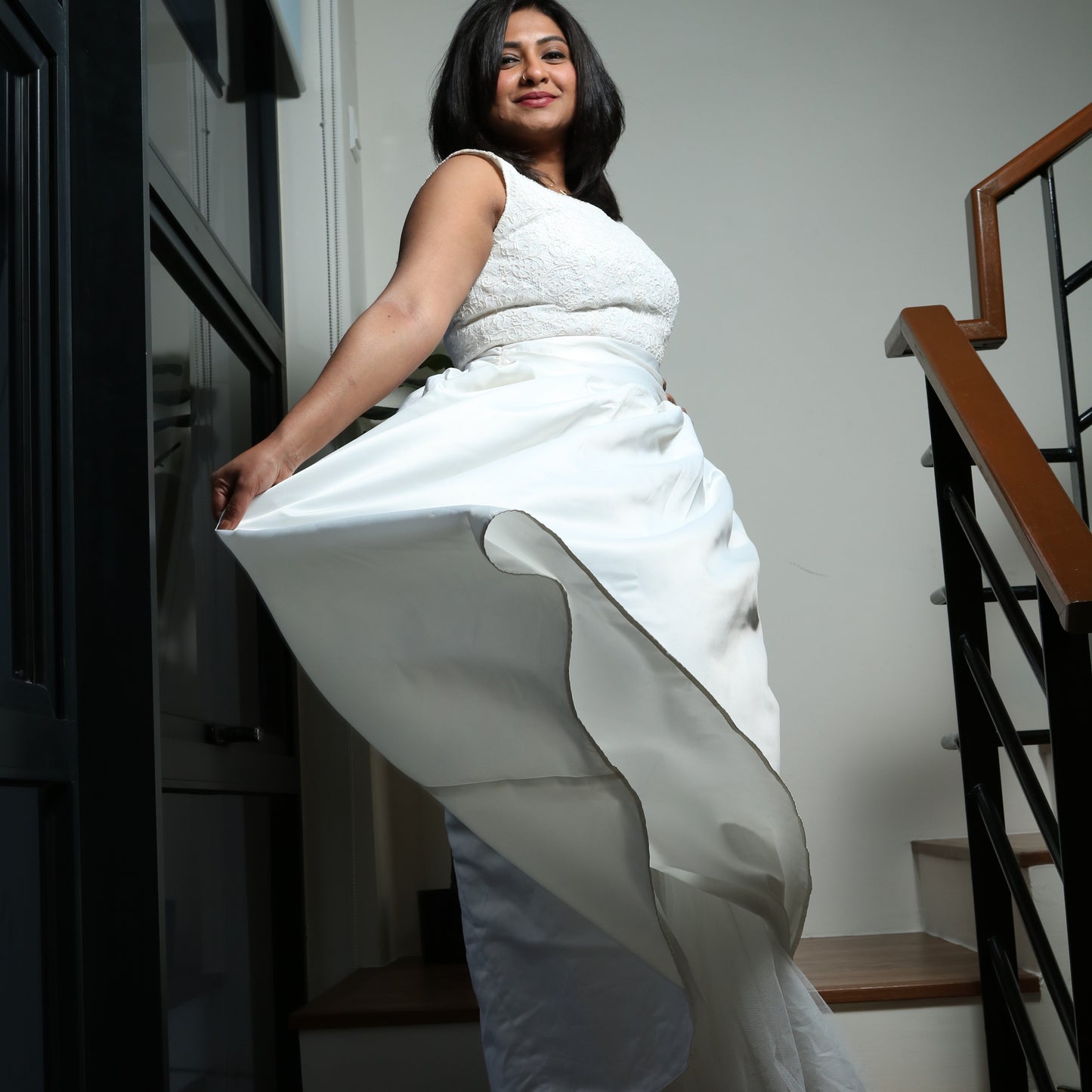 The dress in the image is an elegant white gown featuring a fitted bodice with delicate lace detailing. The sleeveless design enhances its sophisticated appeal, while the full, flowing skirt adds a touch of grace and movement. The structured fabric of the skirt creates a dramatic effect, making it perfect for formal occasions such as weddings, gala events, or special celebrations. The overall look is timeless and refined.