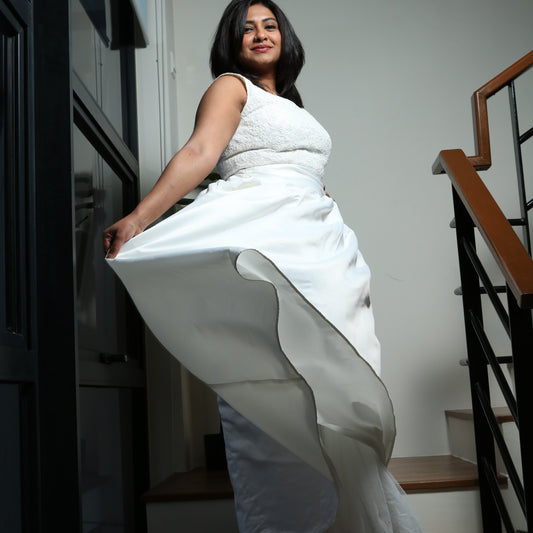 The dress in the image is an elegant white gown featuring a fitted bodice with delicate lace detailing. The sleeveless design enhances its sophisticated appeal, while the full, flowing skirt adds a touch of grace and movement. The structured fabric of the skirt creates a dramatic effect, making it perfect for formal occasions such as weddings, gala events, or special celebrations. The overall look is timeless and refined.