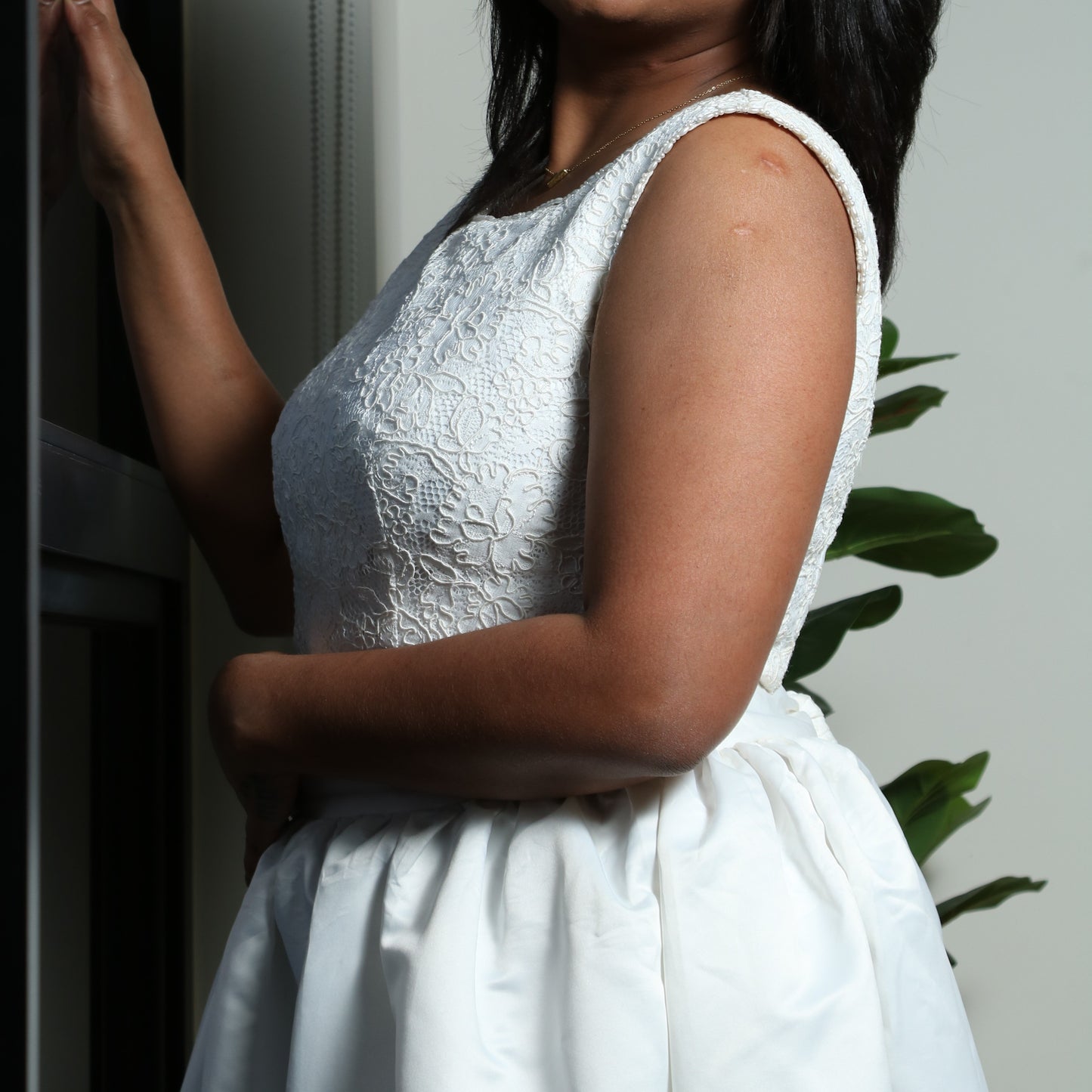 The dress in the image is an elegant white gown featuring a fitted bodice with delicate lace detailing. The sleeveless design enhances its sophisticated appeal, while the full, flowing skirt adds a touch of grace and movement. The structured fabric of the skirt creates a dramatic effect, making it perfect for formal occasions such as weddings, gala events, or special celebrations. The overall look is timeless and refined.
