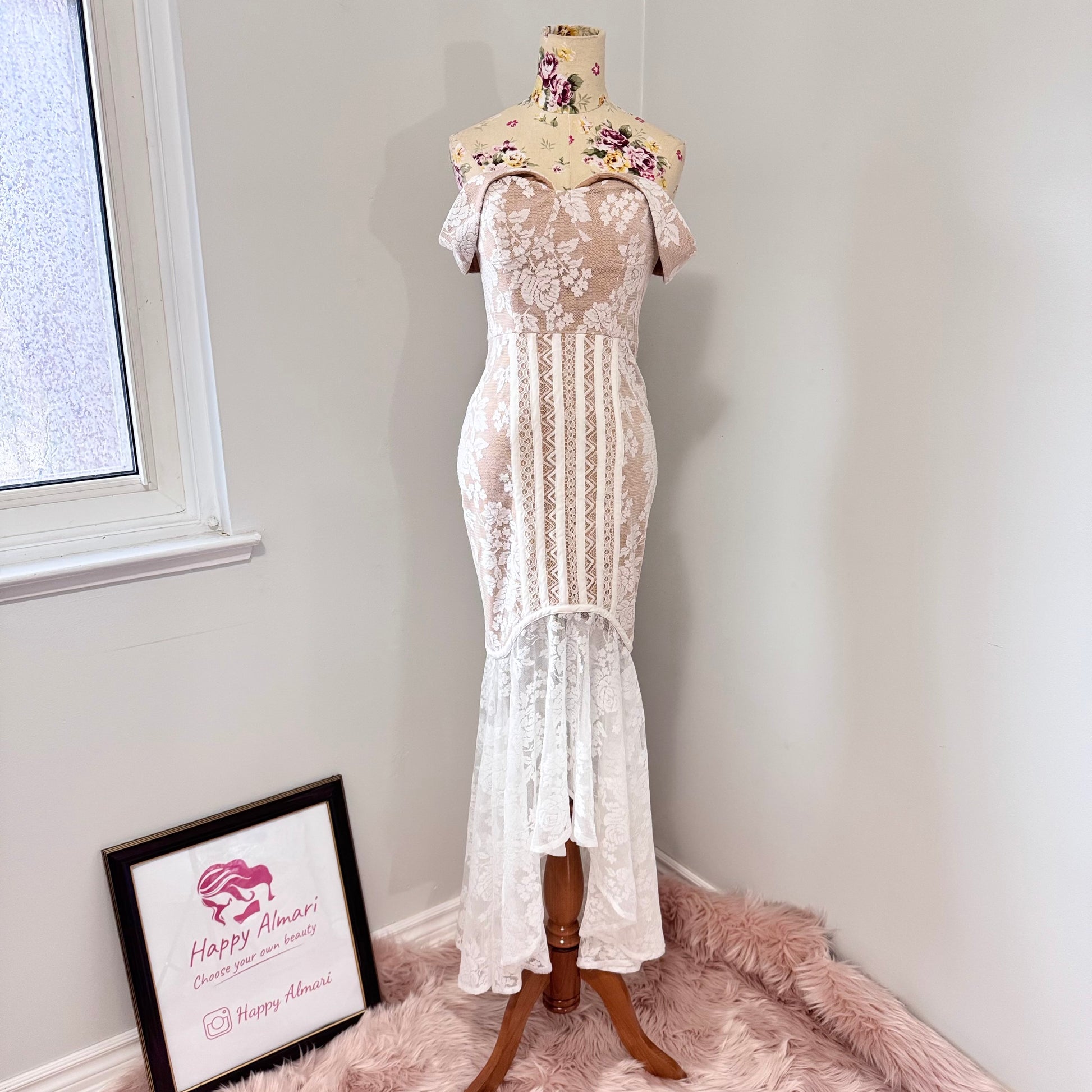 This breathtaking off-shoulder lace gown is designed to captivate with its intricate floral lace detailing and figure-enhancing silhouette. The delicate sheer bodice, complemented by a soft nude underlayer, creates a stunning contrast, while the high-low lace hemline adds a touch of modern romance.