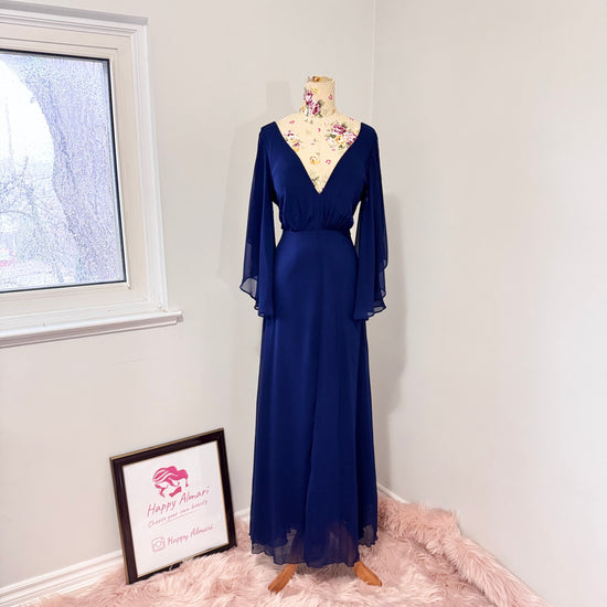 Turn heads in this stunning deep navy gown that radiates elegance and grace. Designed with a flowy chiffon overlay, a flattering cinched waist, and dreamy flutter sleeves, this dress is perfect for formal events, weddings, or special occasions. The deep V-neckline and subtle front slit add just the right touch of sophistication and allure. This gently cherished piece is in excellent condition, ready for a new owner to make unforgettable memories.