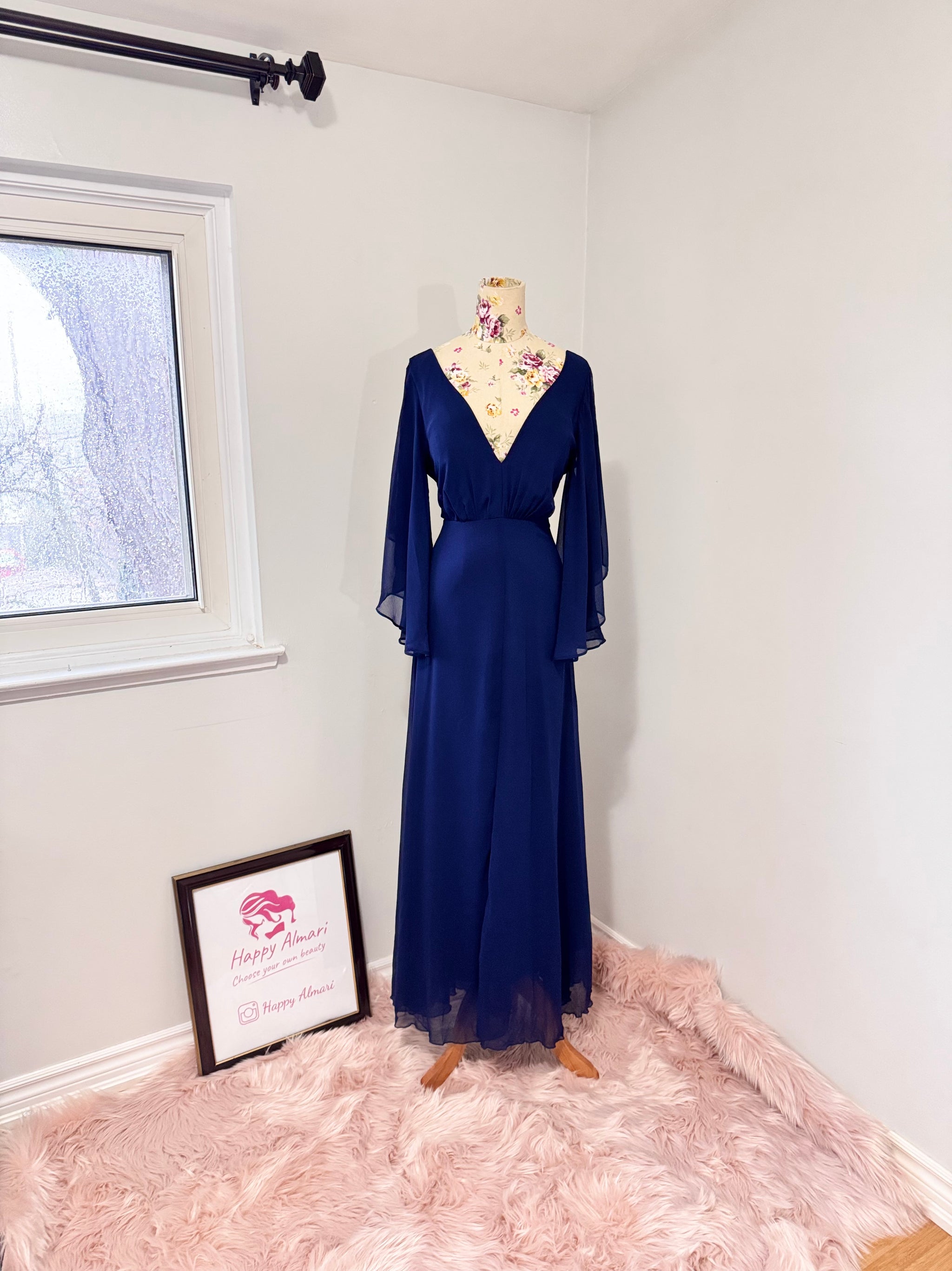 Turn heads in this stunning deep navy gown that radiates elegance and grace. Designed with a flowy chiffon overlay, a flattering cinched waist, and dreamy flutter sleeves, this dress is perfect for formal events, weddings, or special occasions. The deep V-neckline and subtle front slit add just the right touch of sophistication and allure. This gently cherished piece is in excellent condition, ready for a new owner to make unforgettable memories.