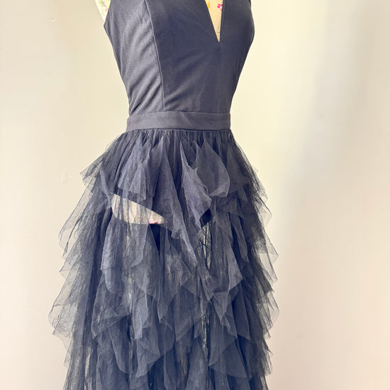Introducing an black tulle gown that exudes timeless sophistication and drama. Featuring a structured, deep V-cut bodice that enhances the silhouette, this piece is designed with a sleek bodysuit bottom for a flawless, sculpted fit. The fitted waistline flows into cascading layers of soft, ruffled tulle, creating a breathtaking, ethereal effect with every step. This beautifully rehomed gown carries a story of style and elegance, ready to be cherished by its next wearer.