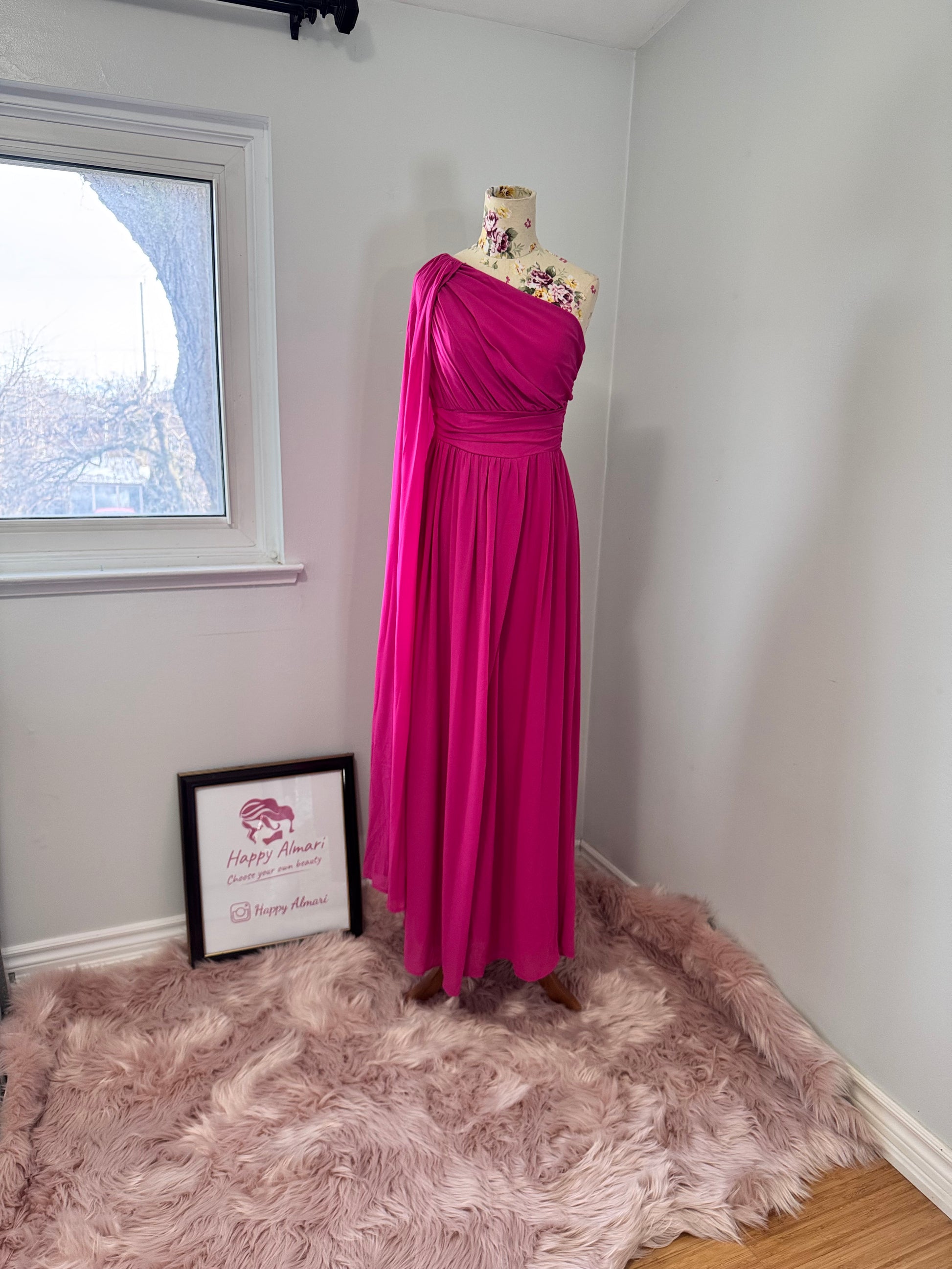Step into effortless elegance with this breathtaking fuchsia one-shoulder gown, designed to make a statement at any event. Featuring a gracefully draped sleeve that cascades like a flowing waterfall, this dress exudes confidence, sophistication, and timeless charm. The cinched waist enhances your silhouette, while the soft, flowing fabric moves beautifully with every step.