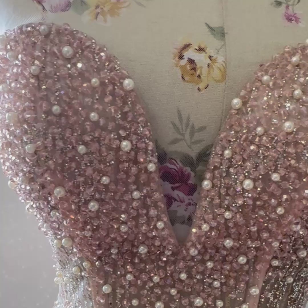 The dress in the image is an elegant, heavily embellished gown with a fitted bodice and a voluminous skirt. It features intricate beadwork and embroidery, giving it a luxurious and opulent look. The sheer illusion neckline adds a delicate touch, while the structured, corset-like bodice enhances the silhouette. The fabric appears to be thick and richly adorned, making the dress quite heavy. The overall design exudes a regal and glamorous feel, perfect for a formal event or gala.