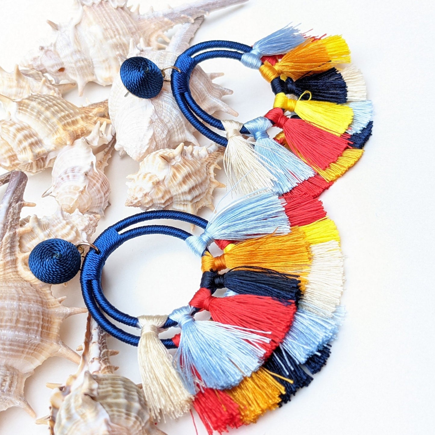 Add a bold pop of color to your look with these tassel earrings, featuring vibrant colours that sway with every move. Lightweight yet eye-catching and made with premium thread, wrapped hoops, and chic fabric-covered studs, they blend comfort with standout style. 